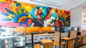 alt="שולחנות-וכיסאות-ועל-הקיר-ציור-קיר-צבעוני-במסעדה-מקסיקנית">