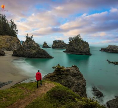 מטייל עומד על צוק וצופה באיים הפזורים באוקיינוס לאורך חוף אורגון הדרמטי במהלך רוד טריפ בארה"ב