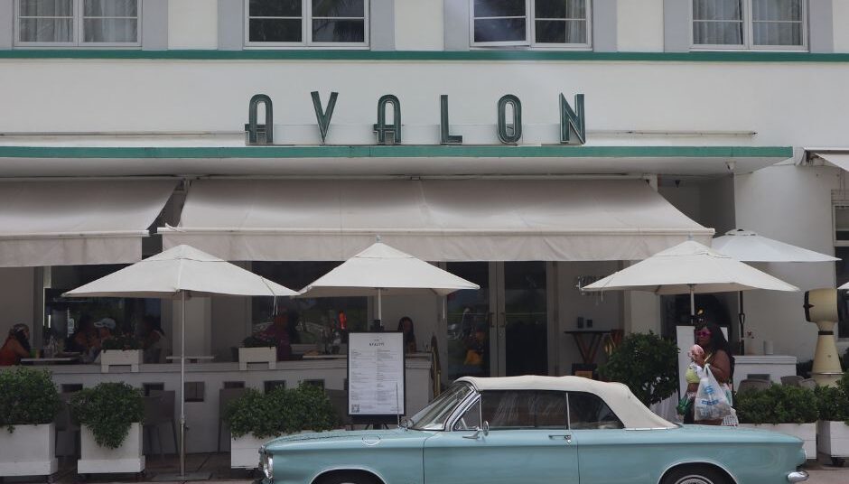 מכונית וינטג' אמריקאית חונה לפני מלון בסגנון אדריכלות ארט דקו (Art Deco) בצבעי פסטל במיאמי פלורידה.